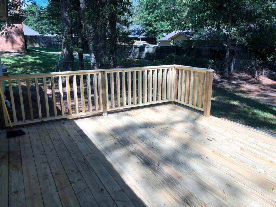 A wooden deck with a railing and trees in the background.