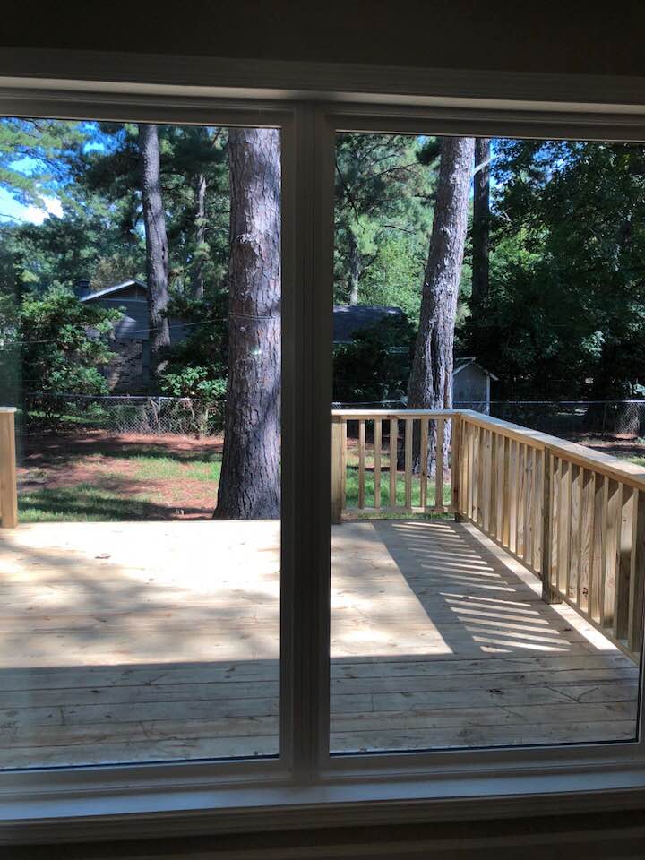 A sliding glass door leading to a wooden deck with trees in the background.