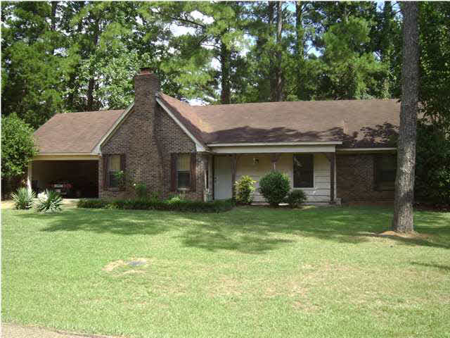 A brick house with a brown roof is surrounded by trees
