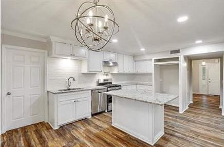 A kitchen with white cabinets , stainless steel appliances , hardwood floors and a chandelier.