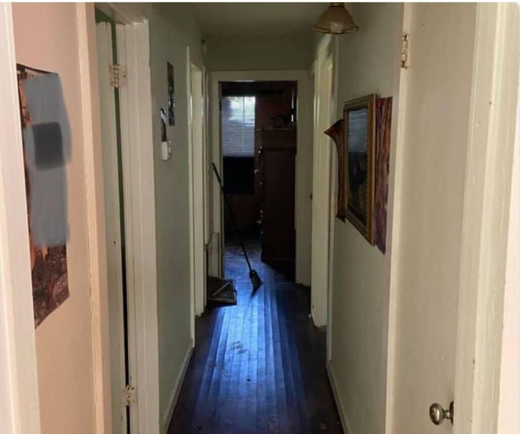 A long hallway with wooden floors and white walls leading to a door.