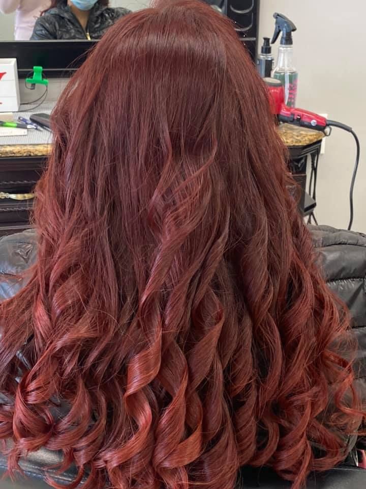 Woman with long, reddish-brown curly hair in a salon.
