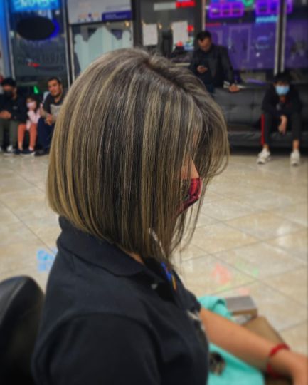 Woman with angled bob haircut, dark with blonde highlights, wearing a mask, in a salon.