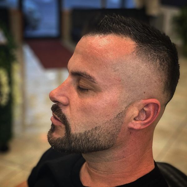 Man with fade haircut and beard, eyes closed. Indoors.
