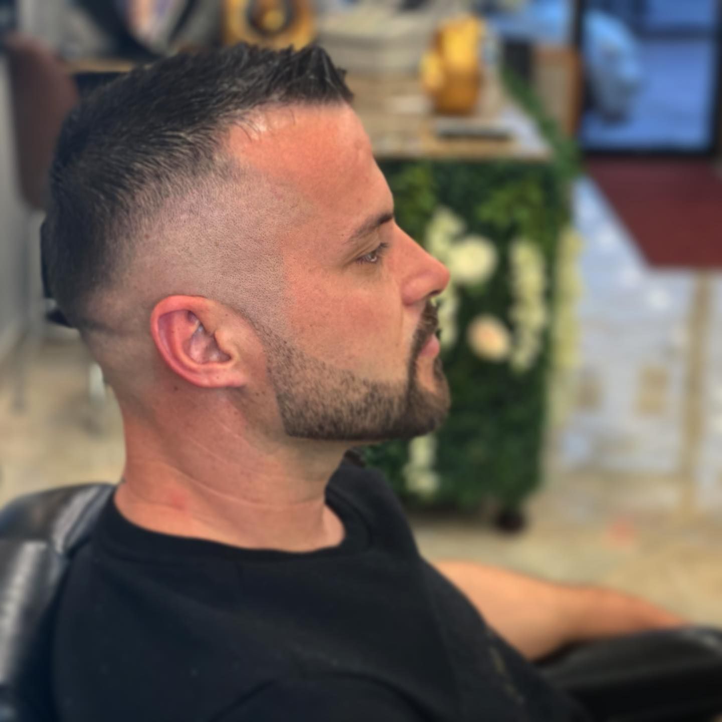Man with short, faded haircut and beard, looking right, in a salon.