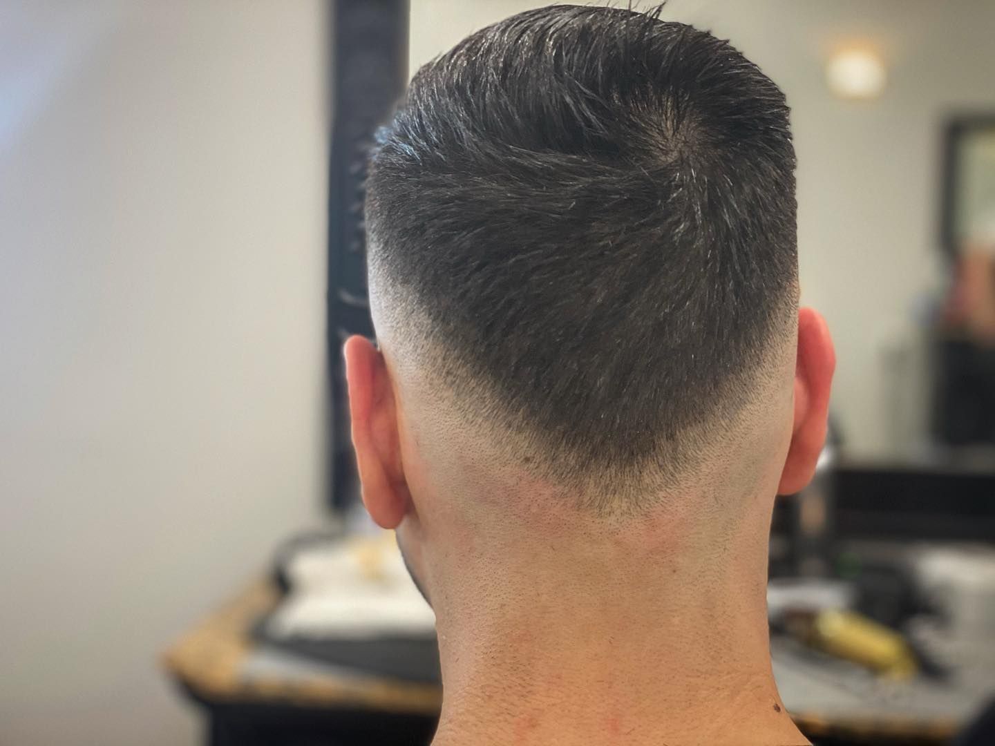 Back of a man's head with a faded haircut, light skin, and dark hair. The hair has a V-shaped taper.
