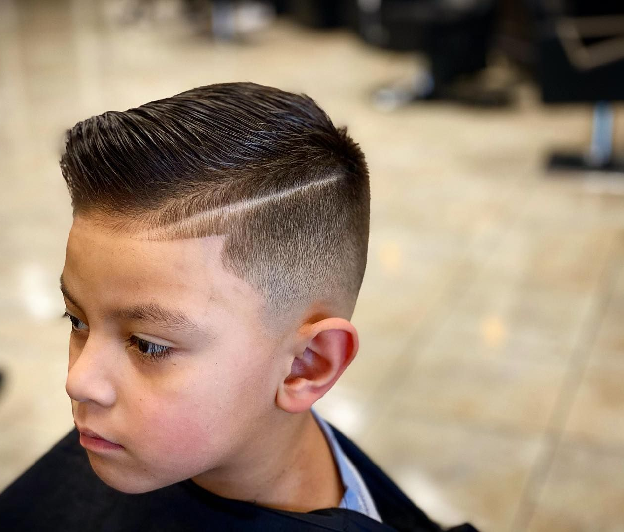 Boy with a faded haircut, comb over, hard part, in a barbershop.