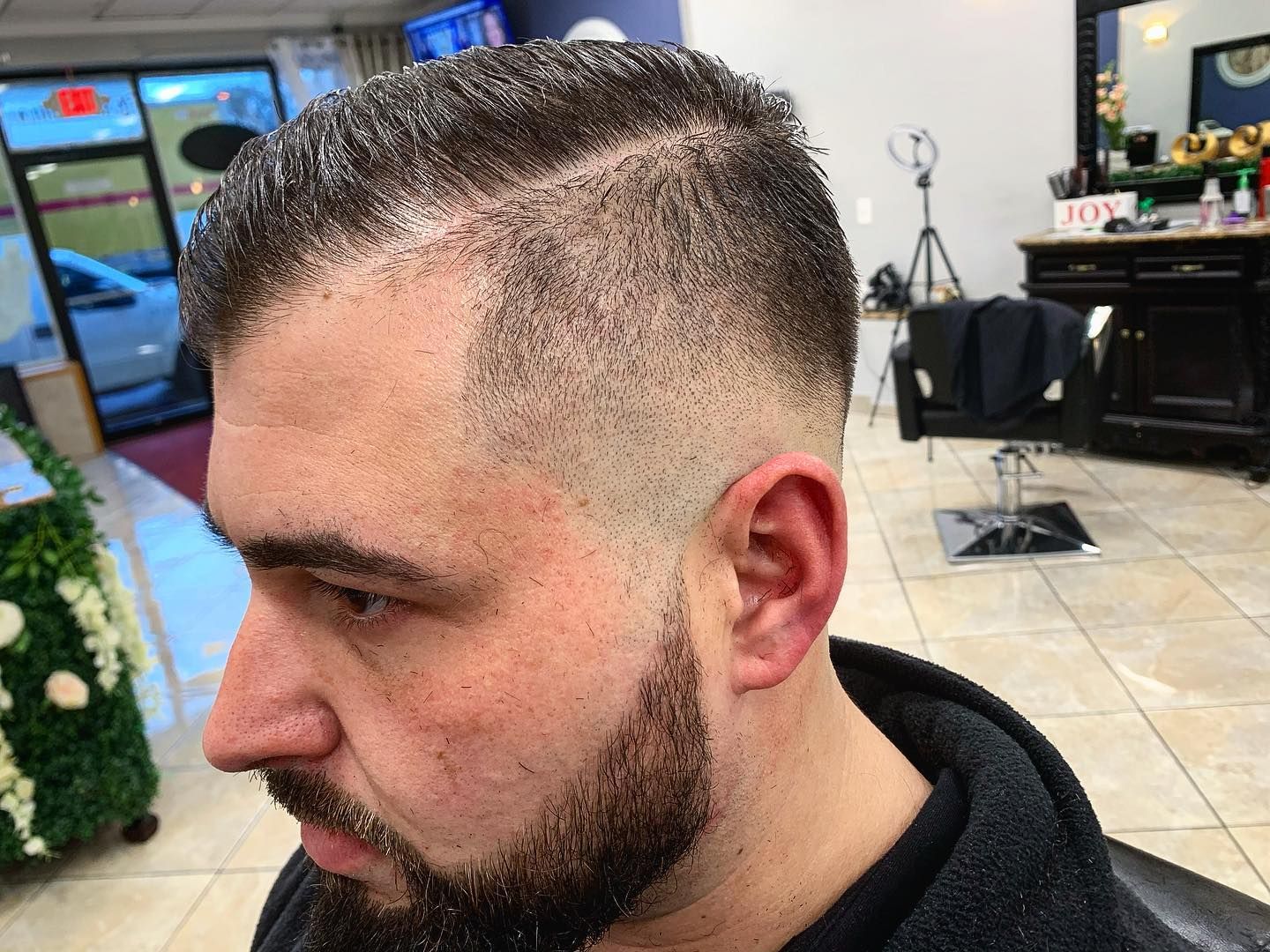 Man with a fade haircut and beard in a salon. Side profile.