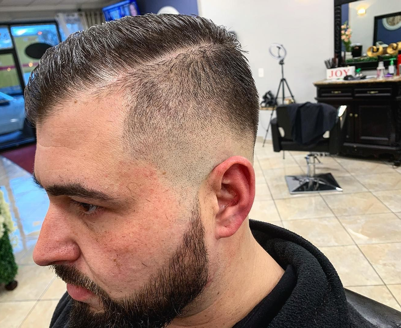 Man with a fade haircut and beard in a barbershop. Dark hair and stubble on the face.