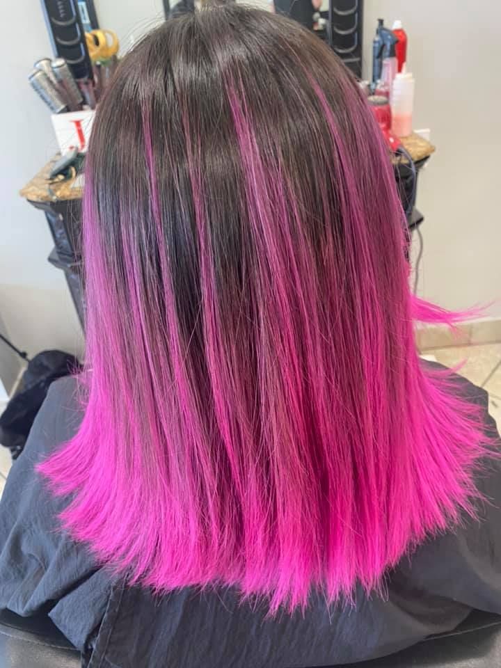 Woman with dark hair, bright pink highlights, in a salon setting.