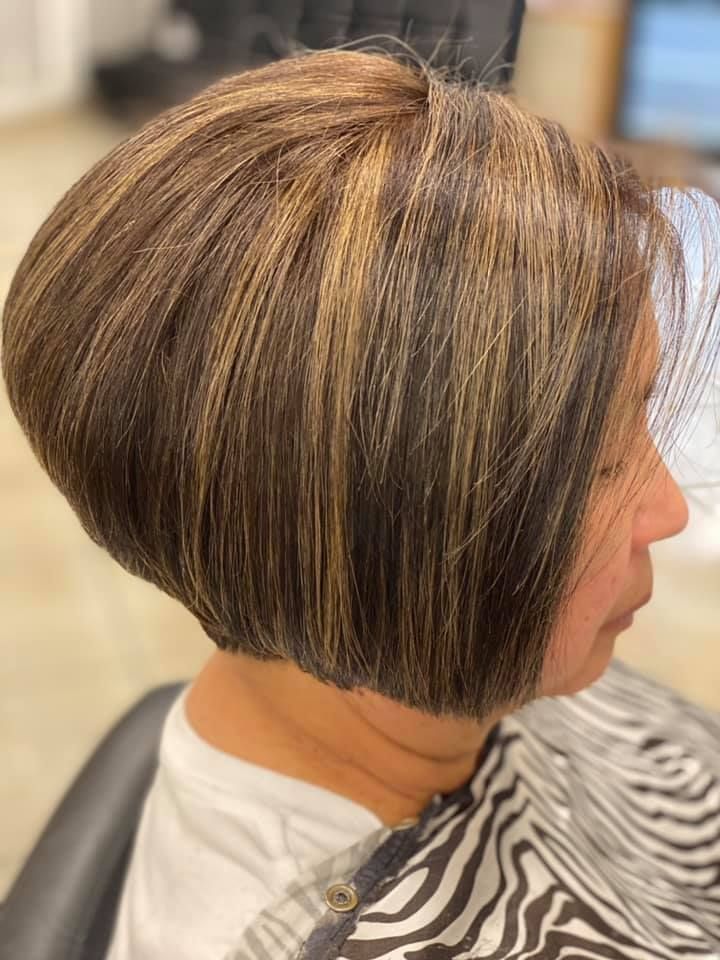 Woman with a stacked, layered bob haircut, brown with blonde highlights. Sitting in a salon chair.