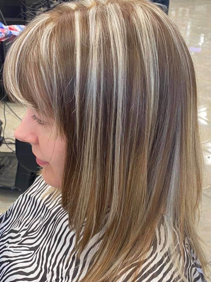 Woman with medium-length layered hair, bangs, and chunky blonde highlights, in a salon chair.