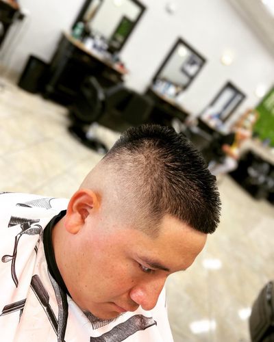Man with a high-fade haircut in a barbershop; light skin, wearing a barber's cape.