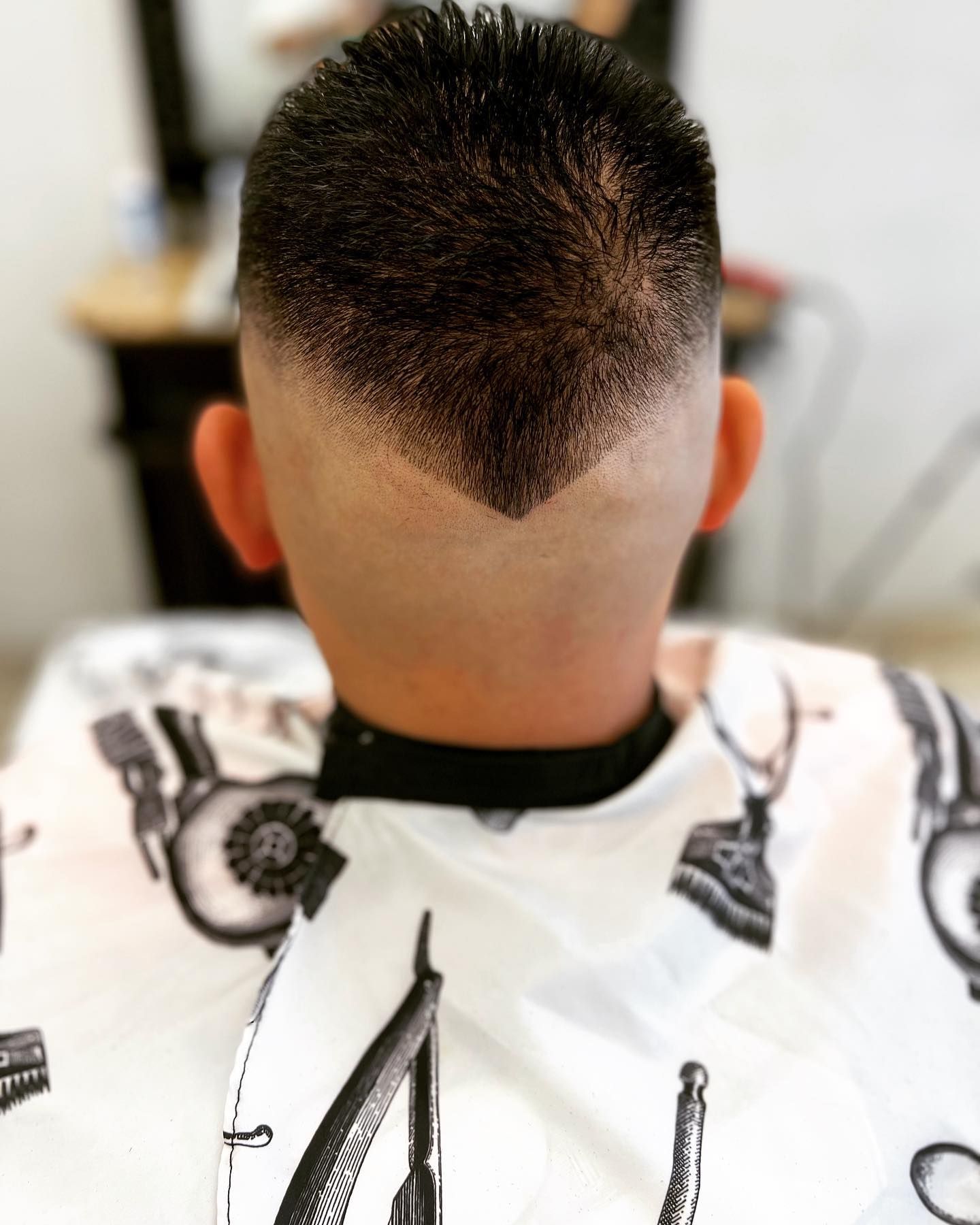 Rear view of a person with a dark, short haircut featuring a V-shaped fade.