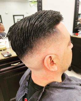 Man with a dark, textured hairstyle, a skin fade haircut. The barber is at work in a salon.