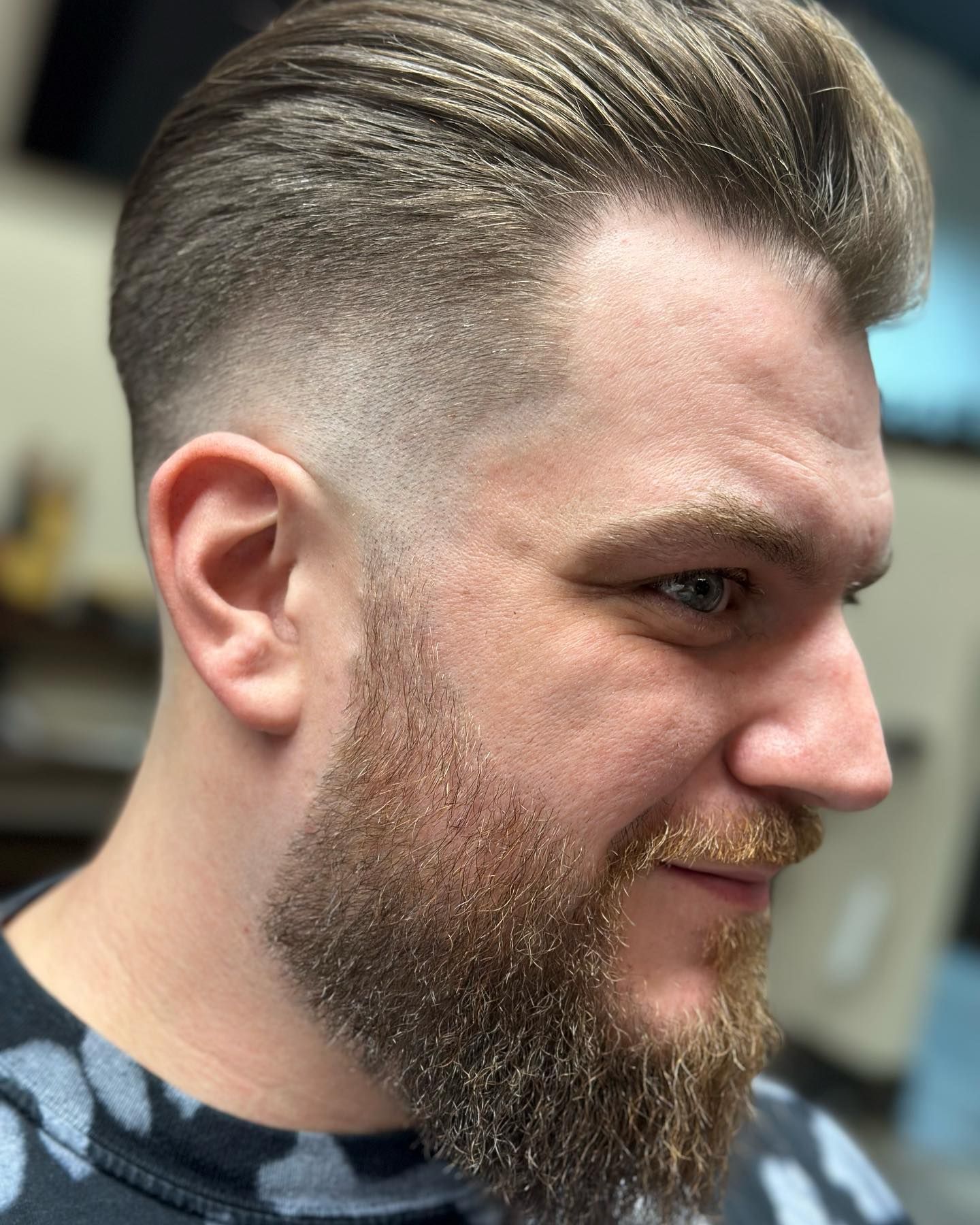 Man with a faded haircut, styled up in front, and a full beard, in an indoor setting.