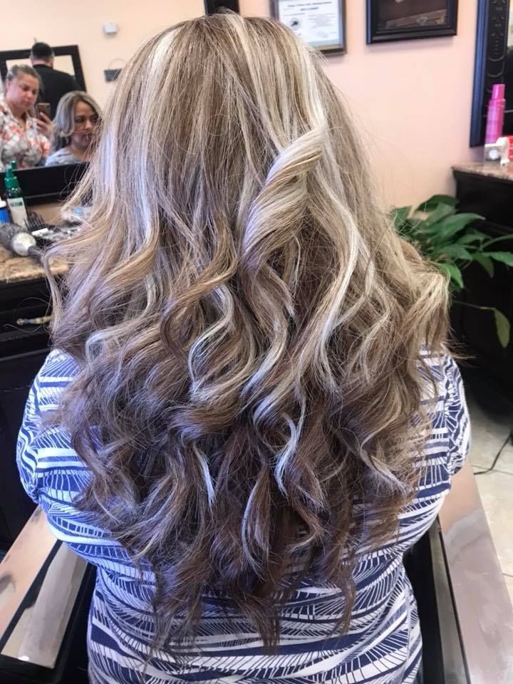 Woman with long, curly hair with blonde highlights, in a salon.