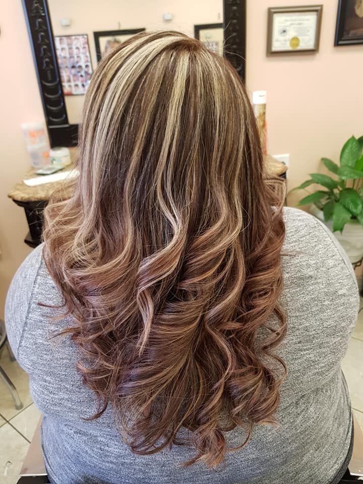 Woman with wavy, highlighted brown hair at a salon. Highlights are blonde, and the ends are a lighter brown/pink.
