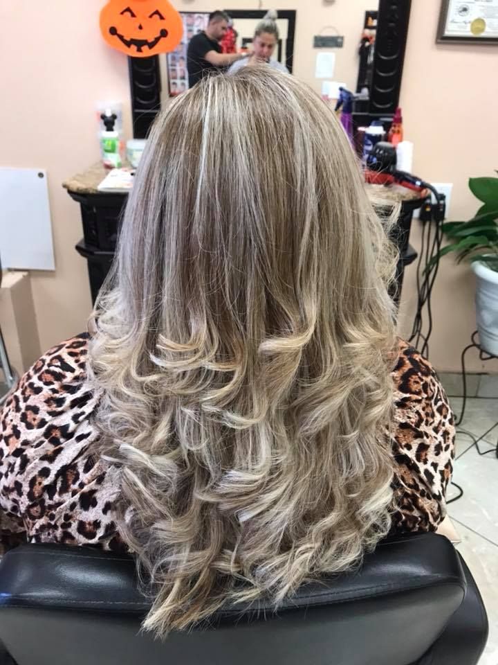 Woman with blonde highlighted, curly hair at a salon, wearing a leopard-print top.