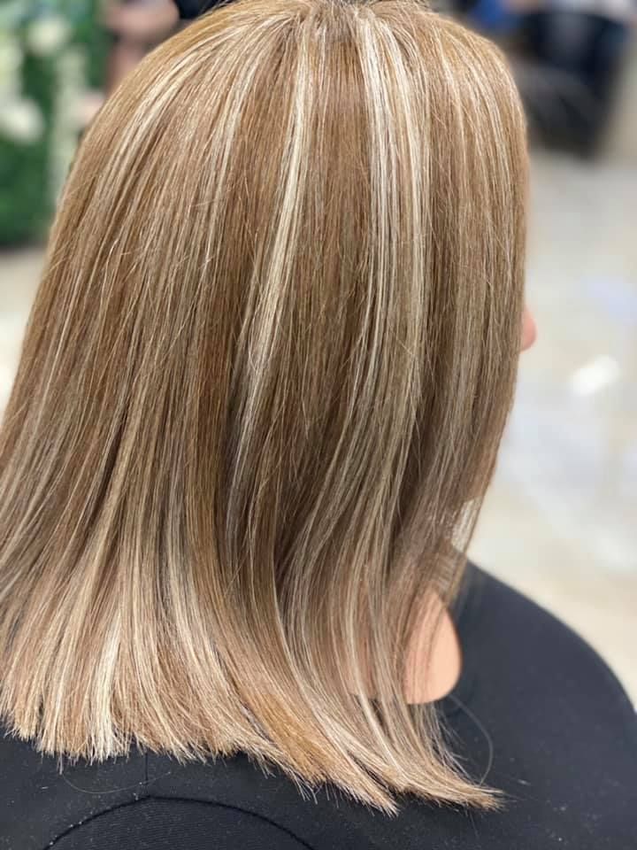 Woman with shoulder-length blonde hair, layered highlights, side view, in salon setting.
