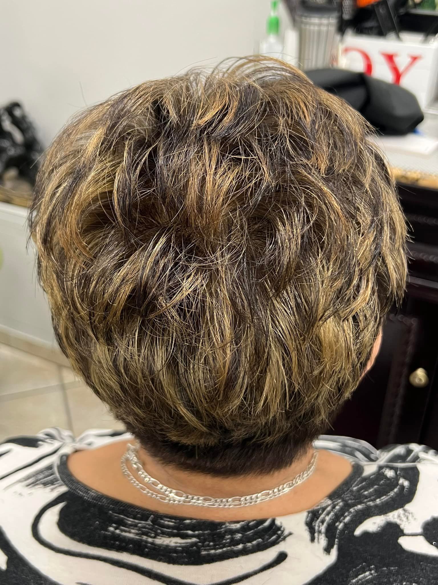 Close-up of woman's short, textured, highlighted hair. She's wearing a black and white patterned top and a necklace.