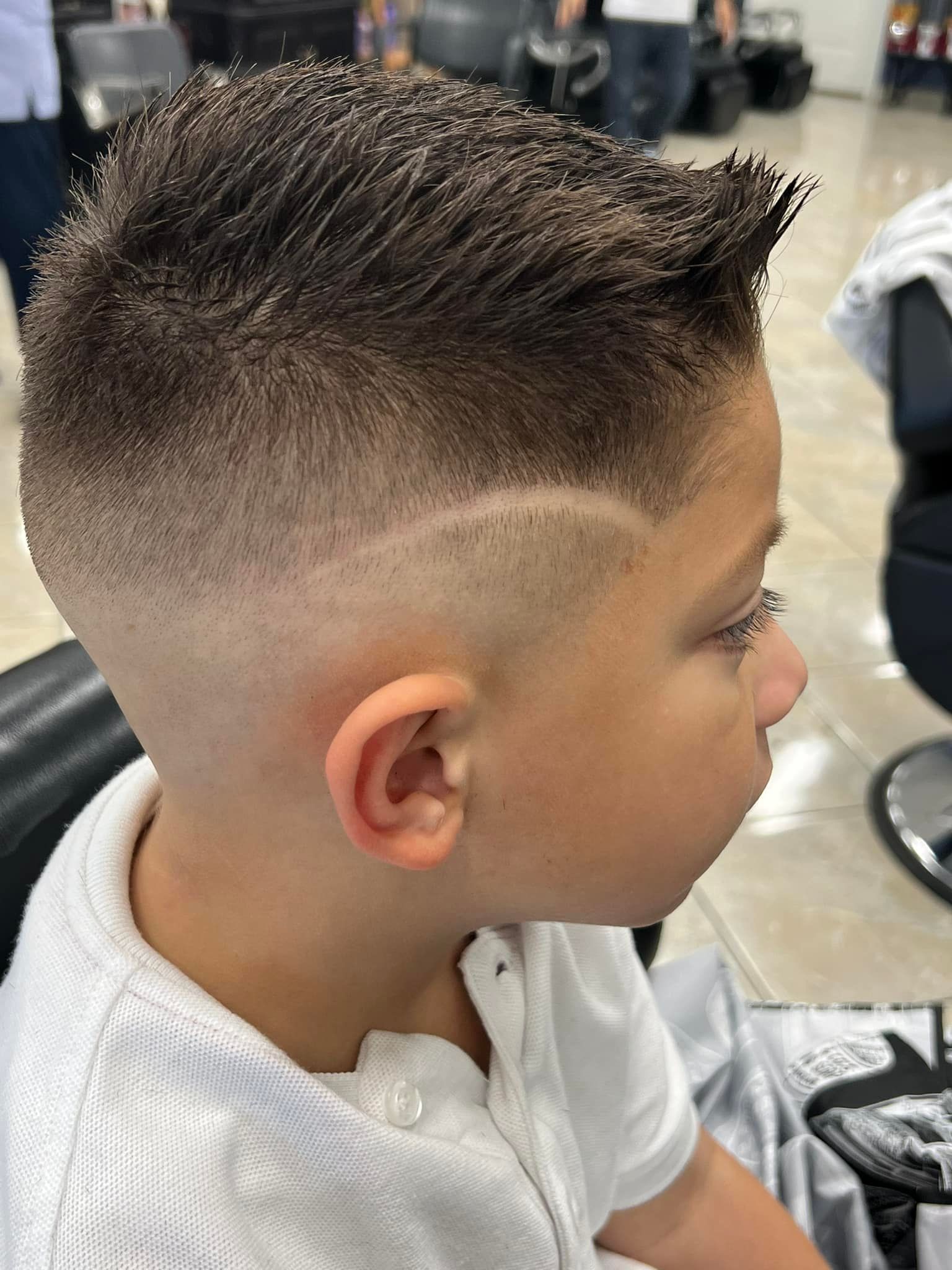Boy with a faded haircut, side part design, and spiky top, sitting in a barber shop.