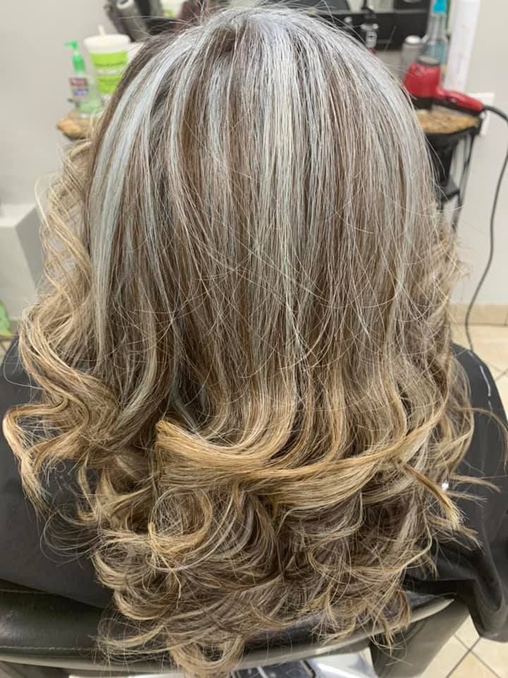 Woman with wavy, highlighted hair in shades of brown, gray, and blonde, in a salon.