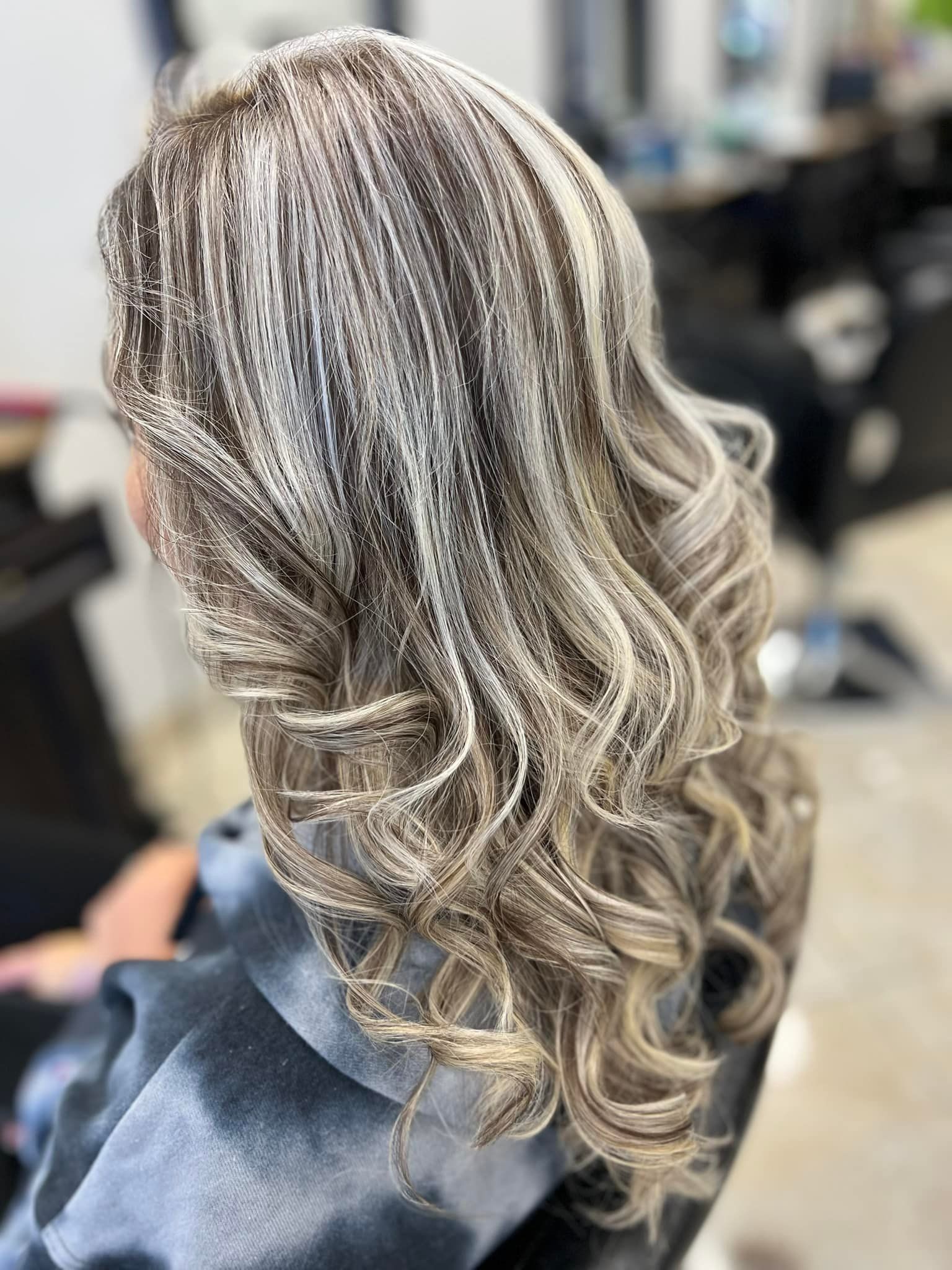 Woman with wavy, light brown hair with blonde highlights, styled at a salon.