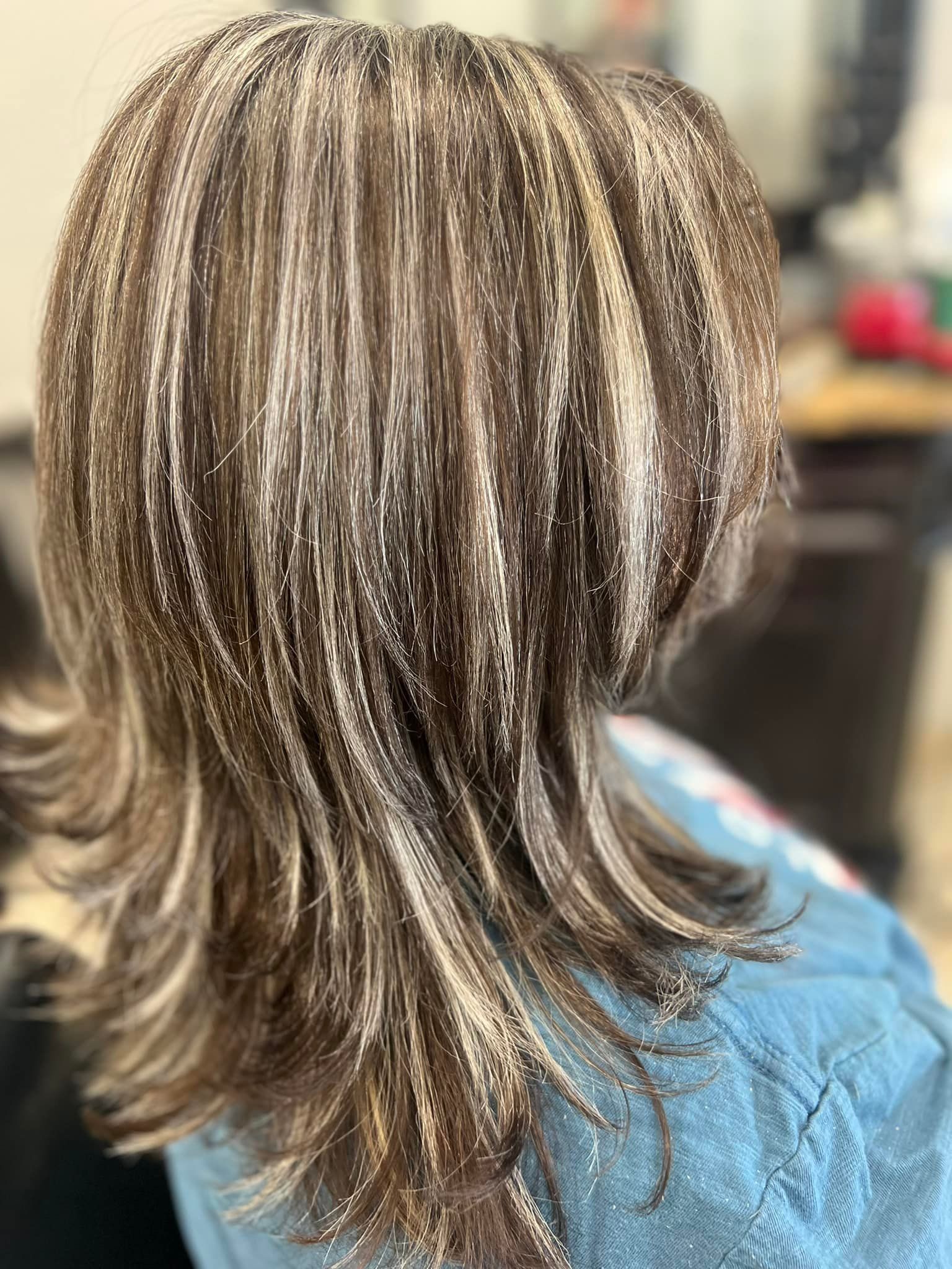 Woman with layered brown hair highlighted with blonde streaks, at a salon.