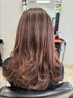 Woman with layered, brown hair with highlights, in a salon chair.