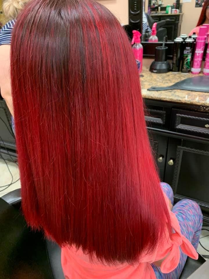 Long, straight red hair, with darker roots, in a salon setting.