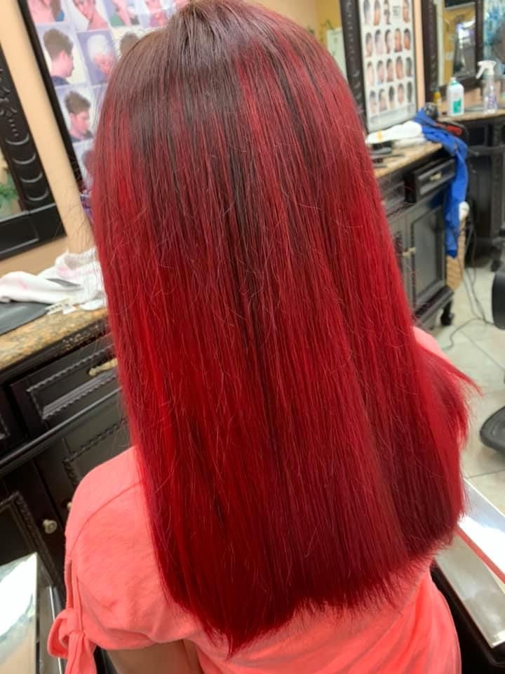 Woman with long, straight red hair in a salon. Hair color is darkest at the roots, fading to bright red.