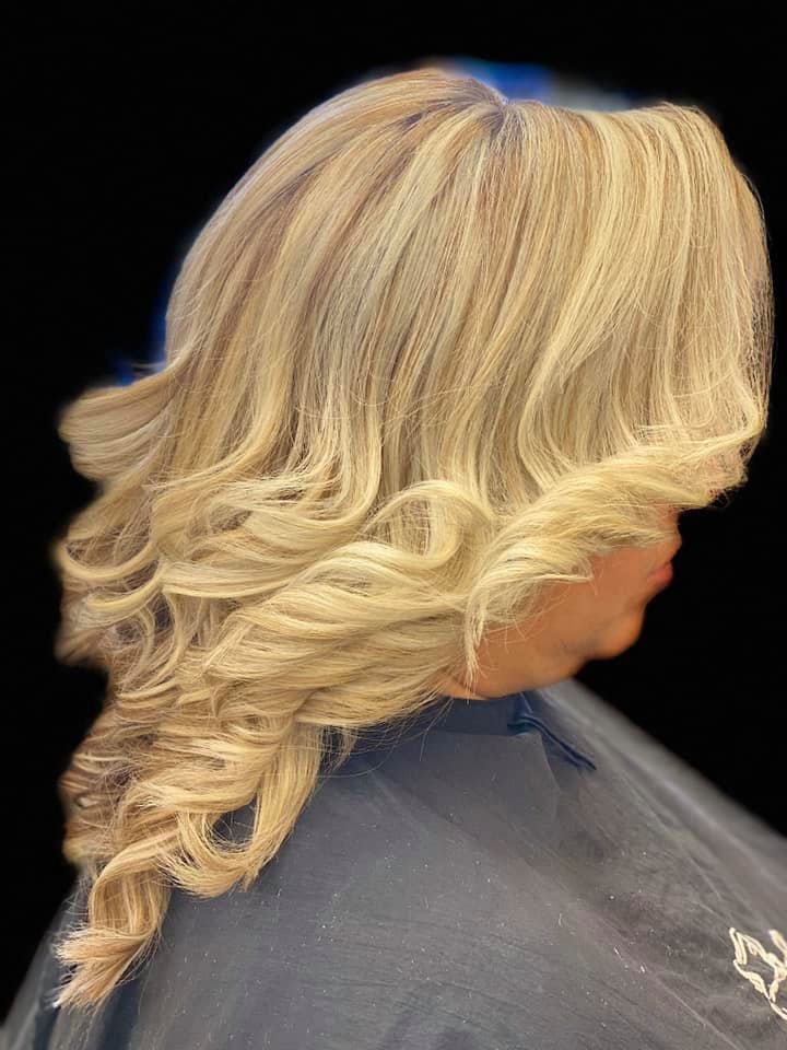 Blonde hair styled in large curls, worn over the shoulder; person in a dark cape.
