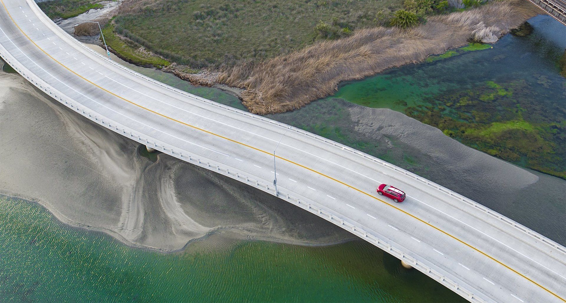 Aerial Drone Photograph of car with surfboard on roof crossing bridge