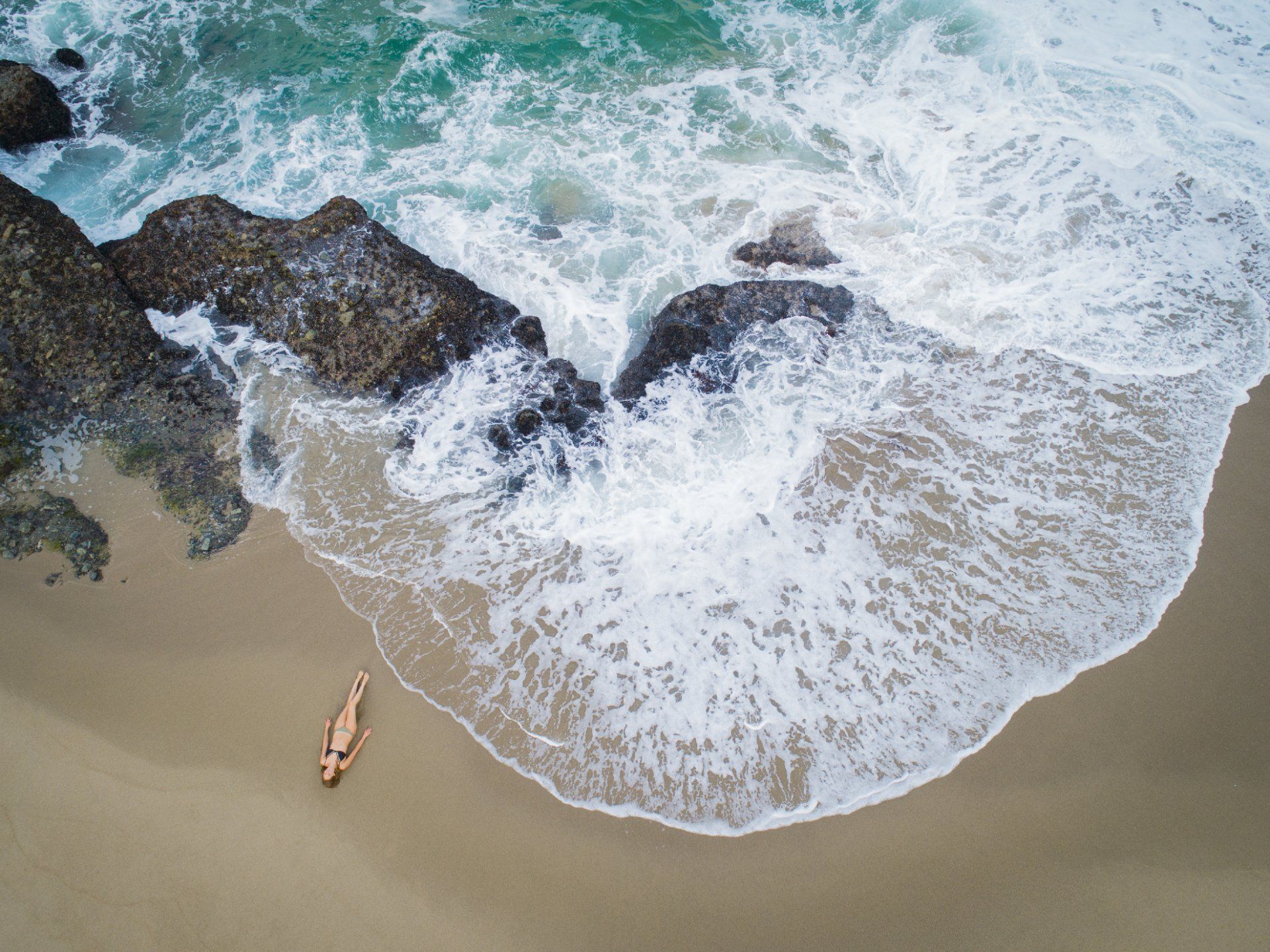 Aerial Drone photograph of woman in bikini laying on rocky beach