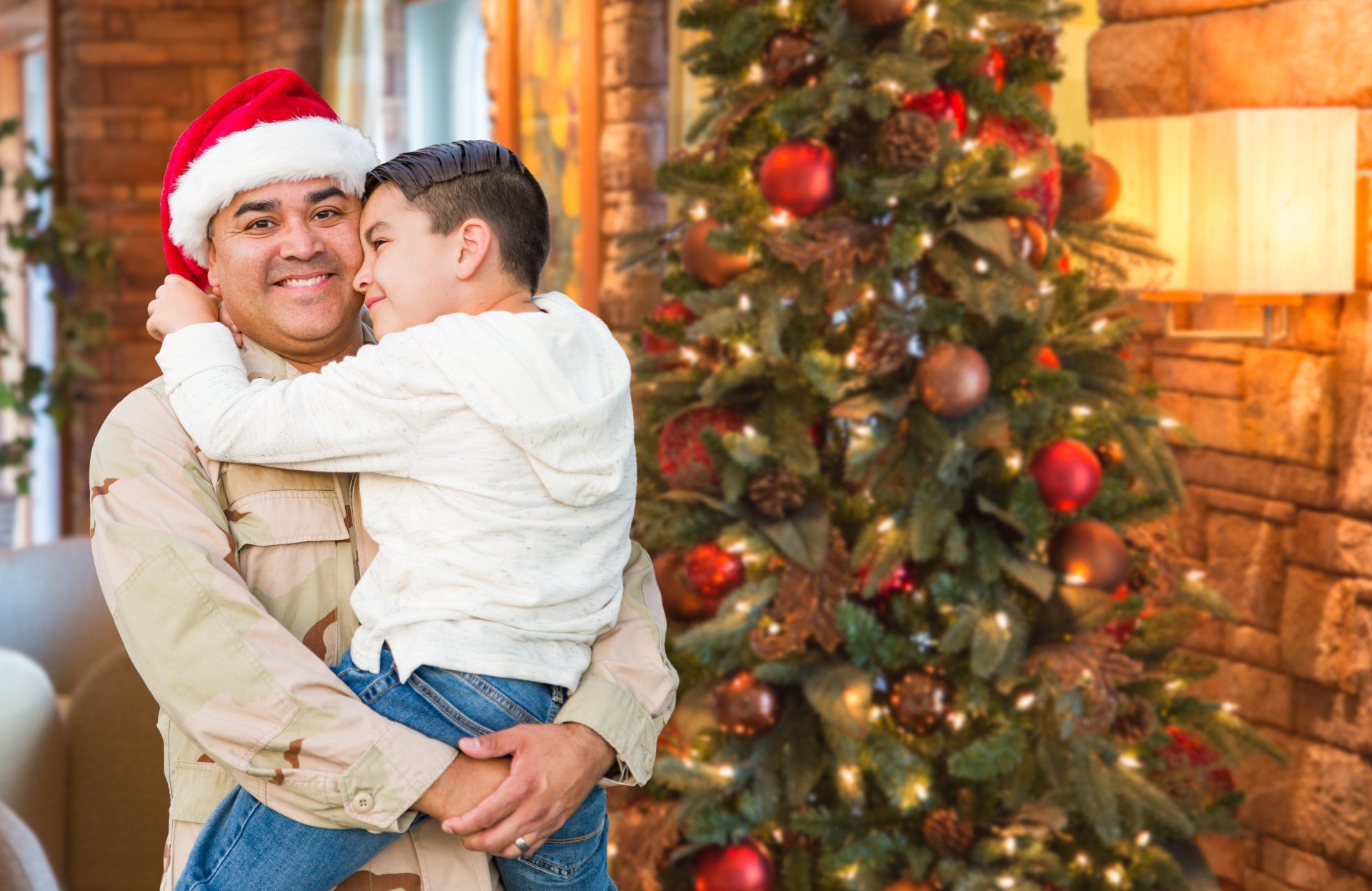 Soldier holding his son by a Christmas tree.