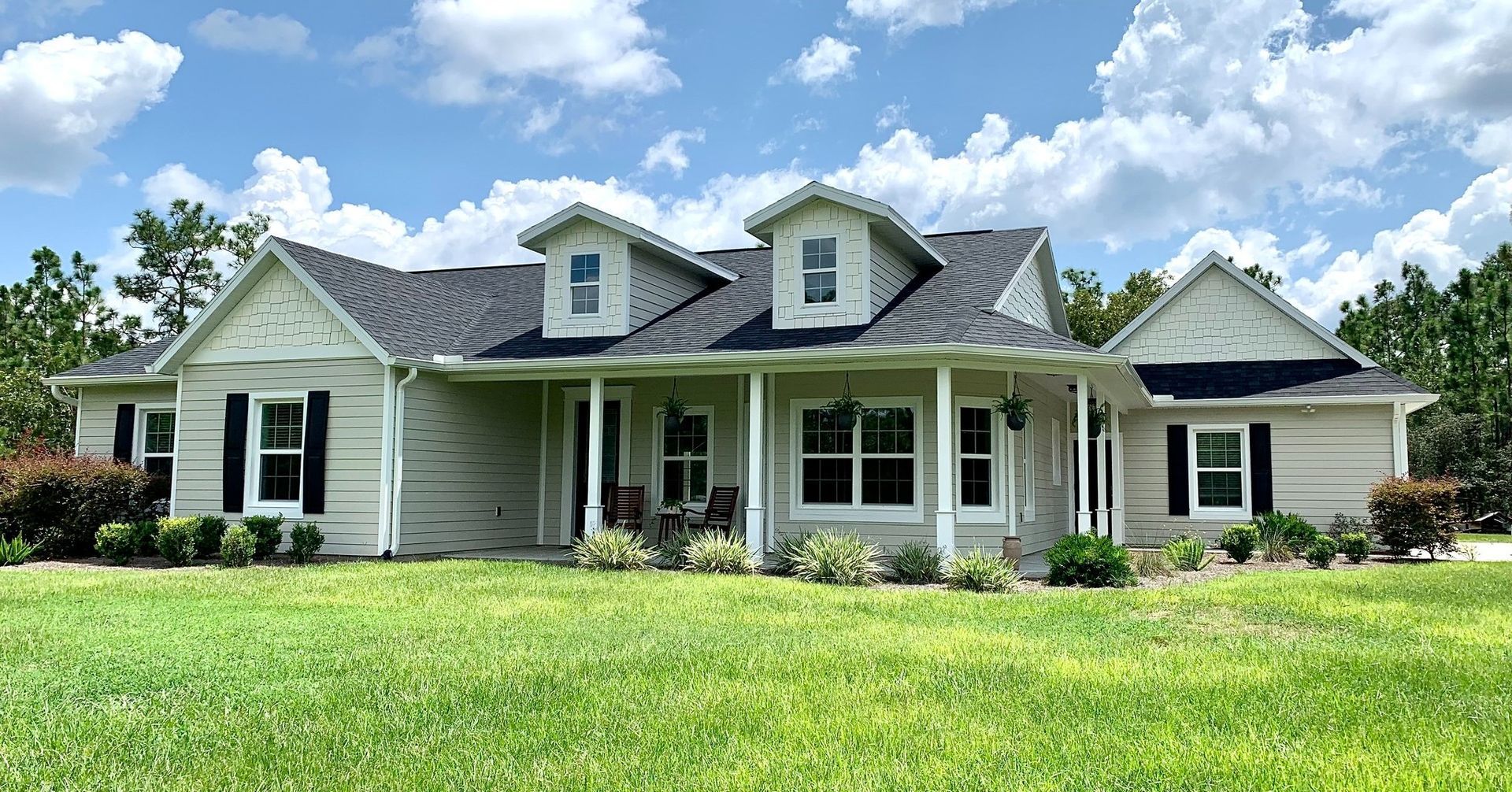 A large white house with a black roof is sitting on top of a lush green field.