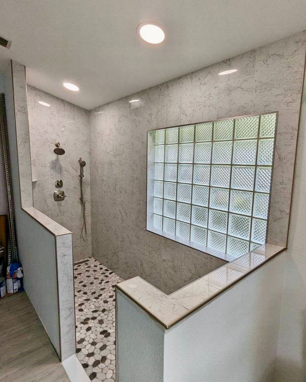 A bathroom with a walk in shower and a glass block window.