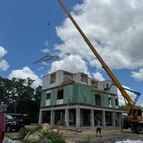 A crane is lifting a roof on a house under construction.