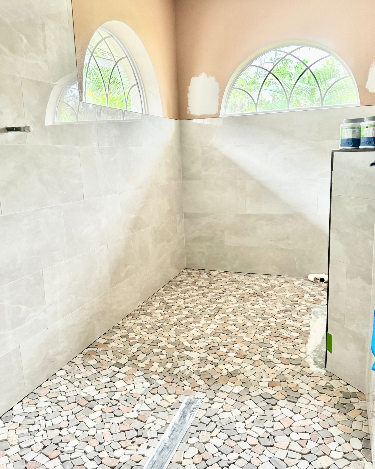 A walk in shower with a tiled floor and a window.