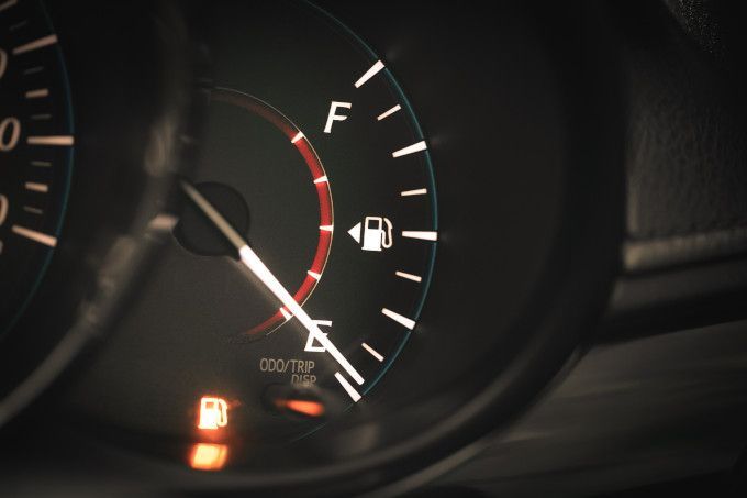 Close-up of a car fuel gauge showing low fuel with the needle near empty and warning light on