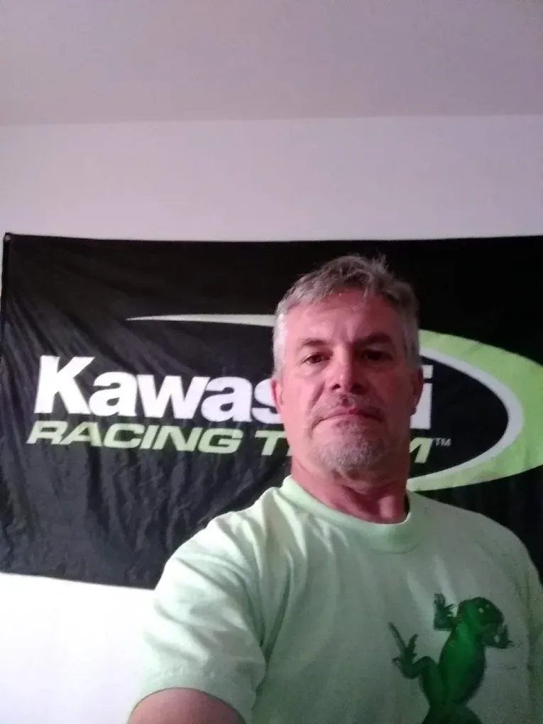 A man taking a selfie in front of a kawasaki racing flag