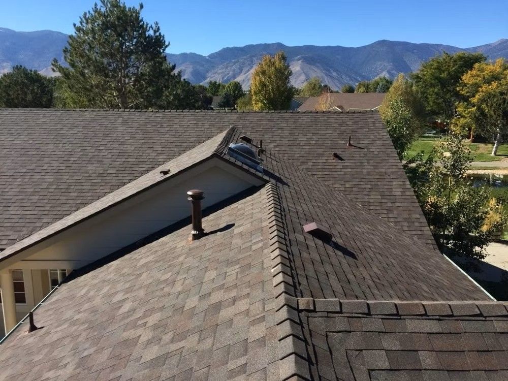 Roof with workers inspecting shingles, mountains and trees in the background Roof with workers inspecting shingles, mountains and trees in the background