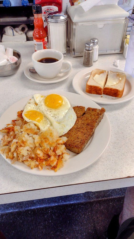 A plate of food with eggs , hash browns , sausage and coffee on a table.