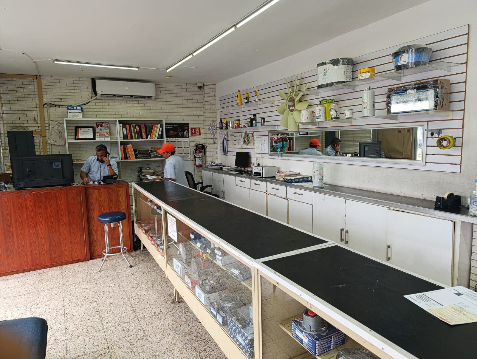 Interior de una tienda de venta de productos electrónicos con dos empleados detrás de mostradores y estantes de exhibición con productos.
