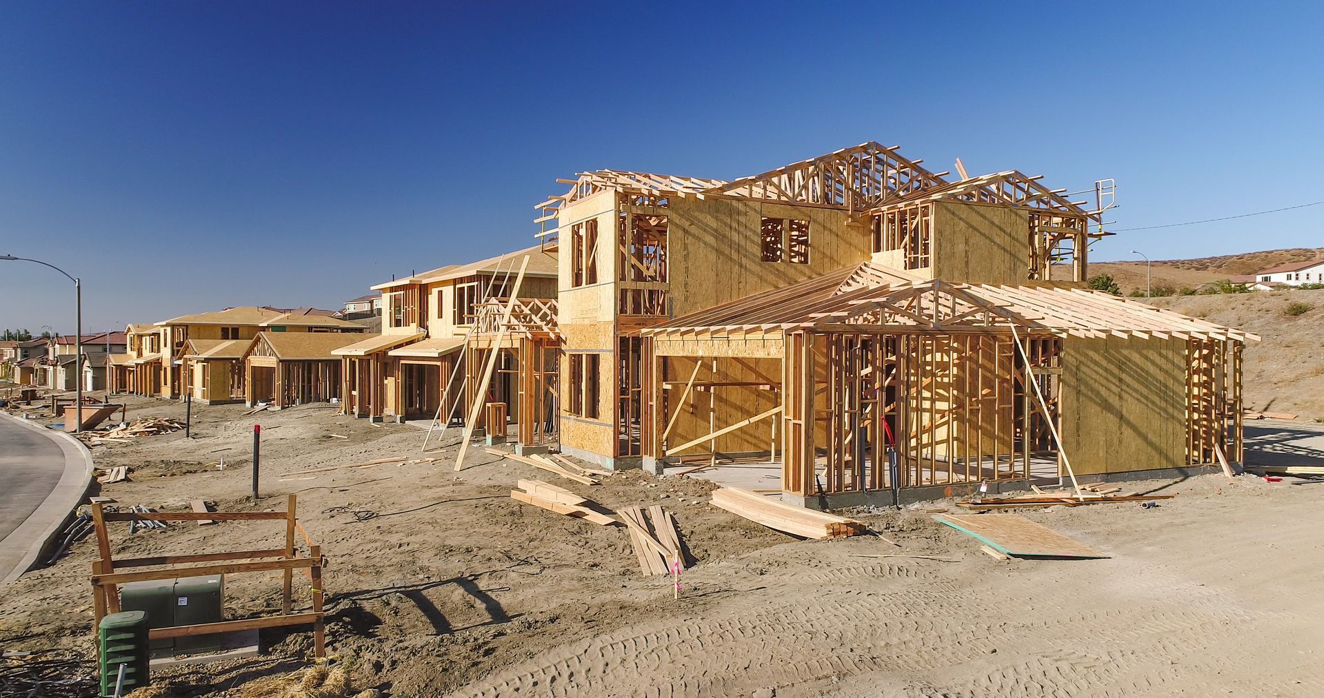 Construction site with wood-framed houses under construction; bright blue sky.
