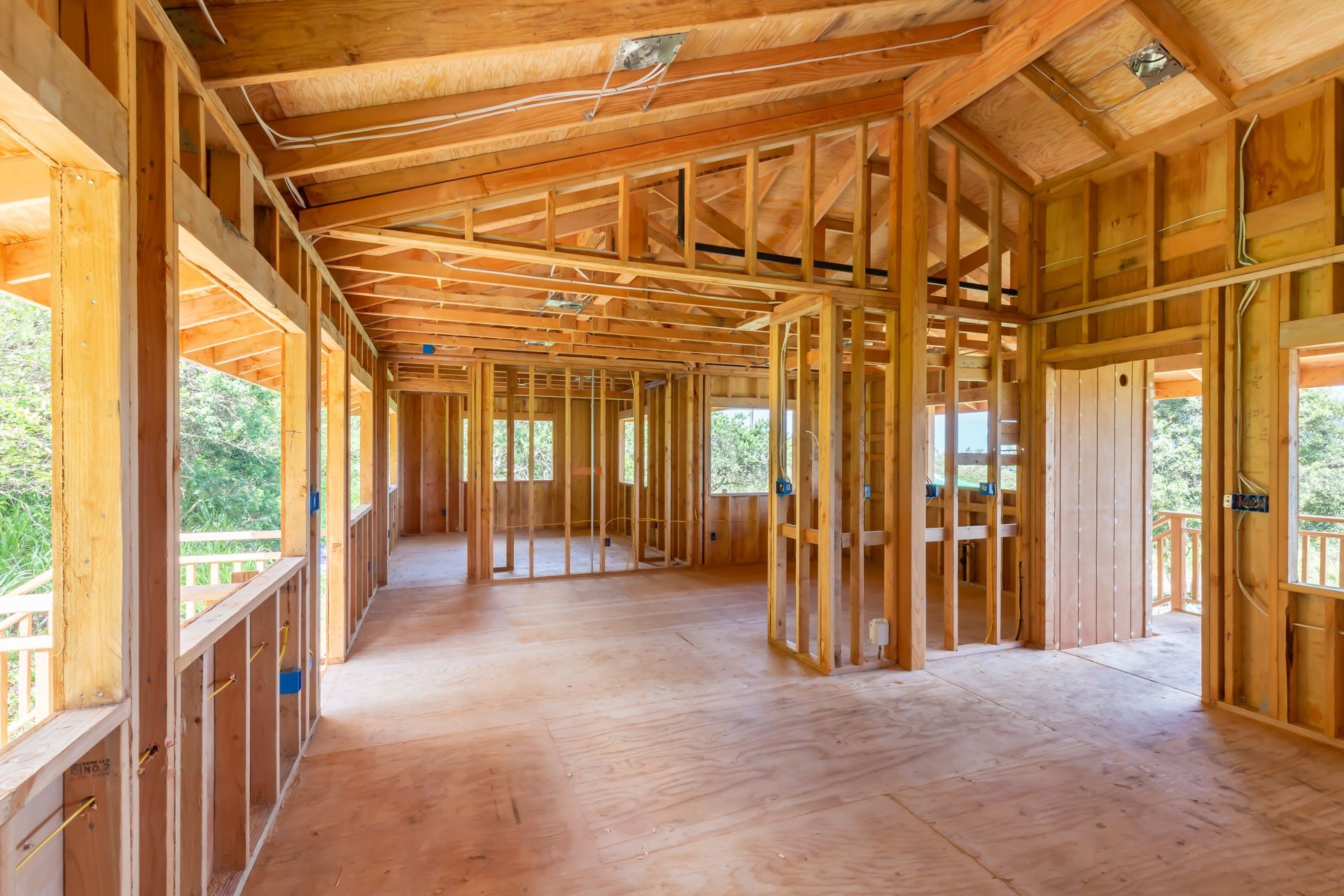 Interior view of a wooden house under construction; exposed framing, windows, and unfinished floors.