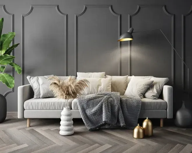 Gray living room with sofa, pillows, throw, plants, lamp, vases on wood floor.