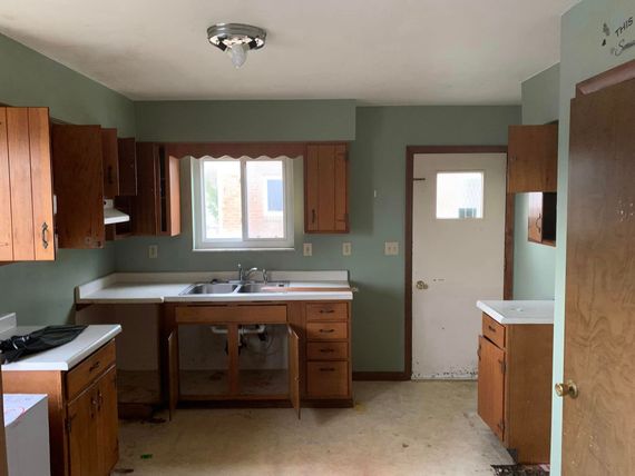 An empty kitchen with wooden cabinets , a sink , and a window.