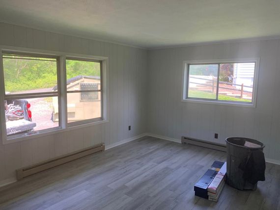 An empty living room with hardwood floors and two windows.